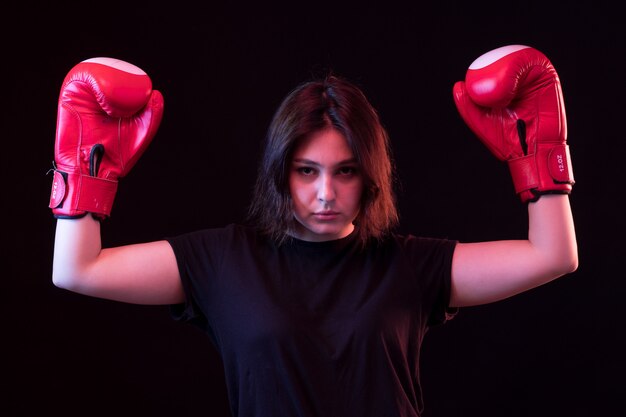 Jovem mulher bonita em camiseta preta e luvas de boxe vermelhas