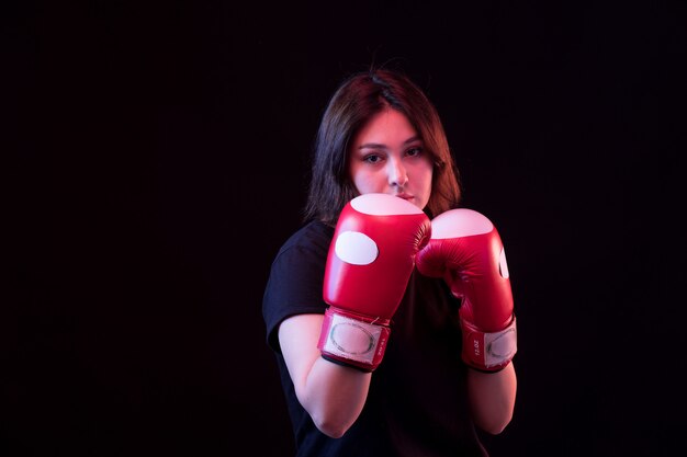 Jovem mulher bonita em camiseta preta e luvas de boxe vermelhas