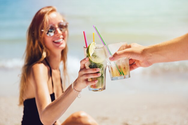 Jovem mulher bonita em óculos de sol e maiô, brindando com coquetel