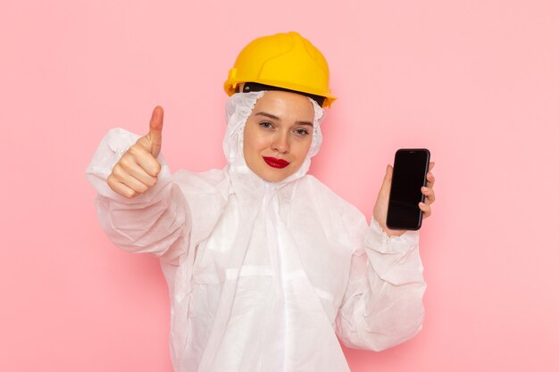 jovem mulher bonita em um terno branco especial e capacete amarelo segurando o telefone com um sorriso rosa