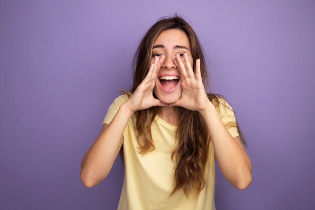 Jovem mulher bonita em uma camiseta bege feliz e animada gritando com as mãos perto da boca