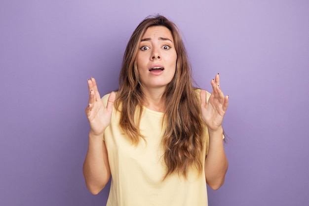 Jovem mulher bonita em uma camiseta bege olhando para a câmera preocupada e assustada levantando os braços