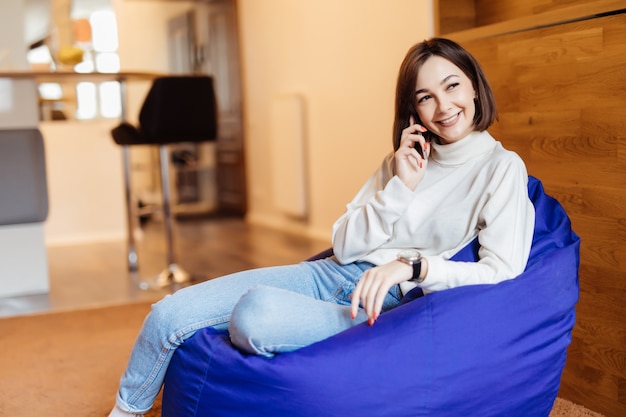 Jovem mulher bonita está sentada na cadeira violeta brilhante usando seu telefone mensagens de texto