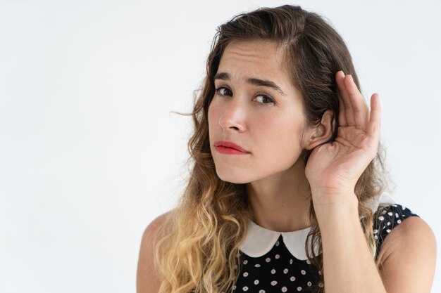 Jovem mulher bonita focalizada que guarda a mão perto da orelha e que olha a câmera.