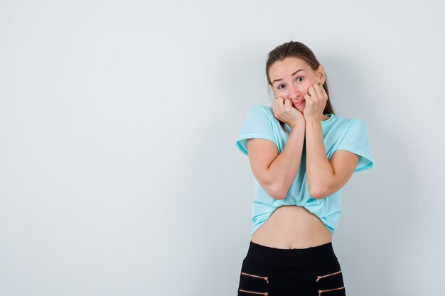 Jovem mulher bonita no rosto de almofada de t-shirt nas mãos e olhando pensativa, vista frontal.