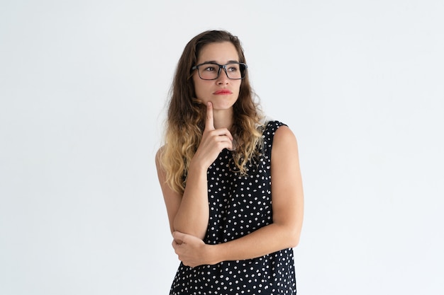 Foto grátis jovem mulher bonita pensativa que toca no queixo com dedo e que olha afastado.