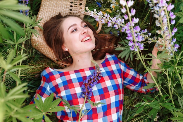 Jovem mulher bonita que encontra-se no campo na grama verde e nas flores.