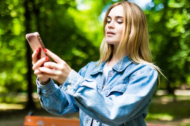 Jovem mulher bonita senta-se num banco do parque, verifica o telefone. Ao ar livre.