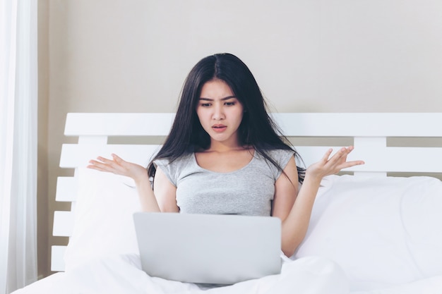 Jovem mulher bonita sentada na cama, ela usa o laptop e se sente sério e triste