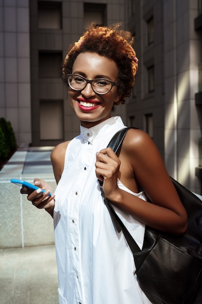 Jovem mulher bonita sorrindo segurando o telefone andando pela cidade