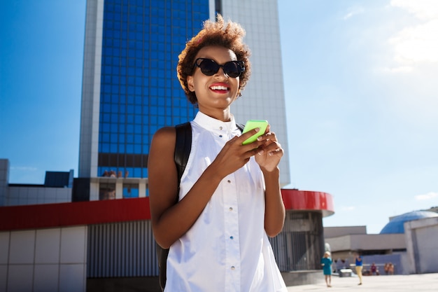 Foto grátis jovem mulher bonita sorrindo segurando o telefone andando pela cidade