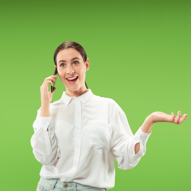 Jovem mulher bonita usando telefone celular na parede de cor verde. conceito de emoções faciais humanas.