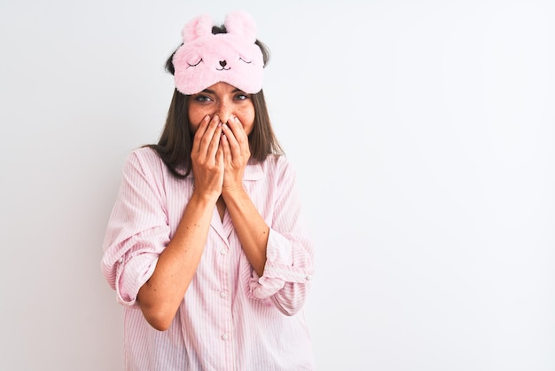 Jovem mulher bonita vestindo máscara de dormir e pijama sobre fundo branco isolado rindo e rindo envergonhado cobrindo a boca com fofocas de mãos e conceito de escândalo