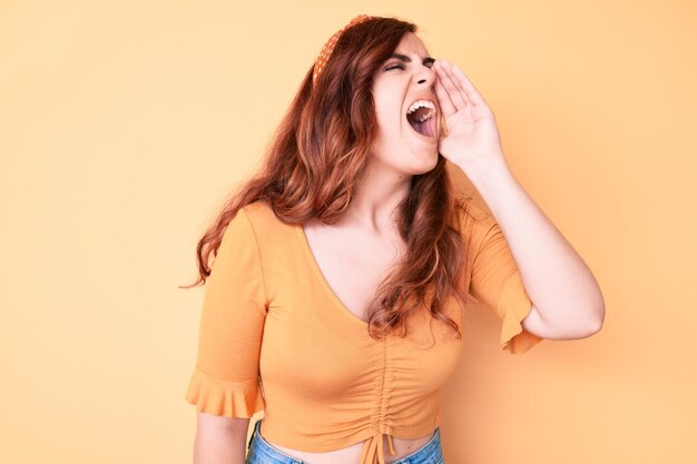 Jovem mulher bonita vestindo roupas casuais gritando e gritando alto a lado com a mão na boca. conceito de comunicação.