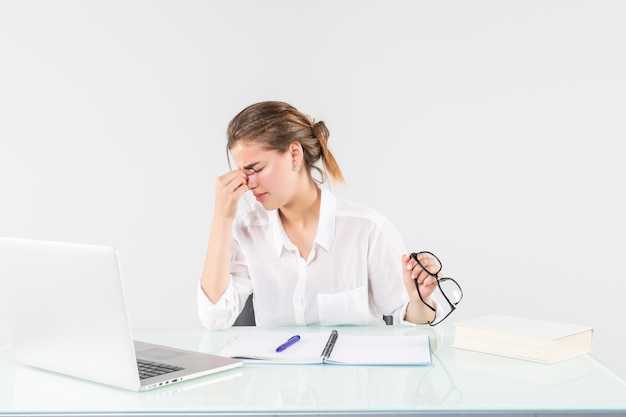 Jovem mulher cansada na frente de um laptop na mesa de escritório, isolada no fundo branco