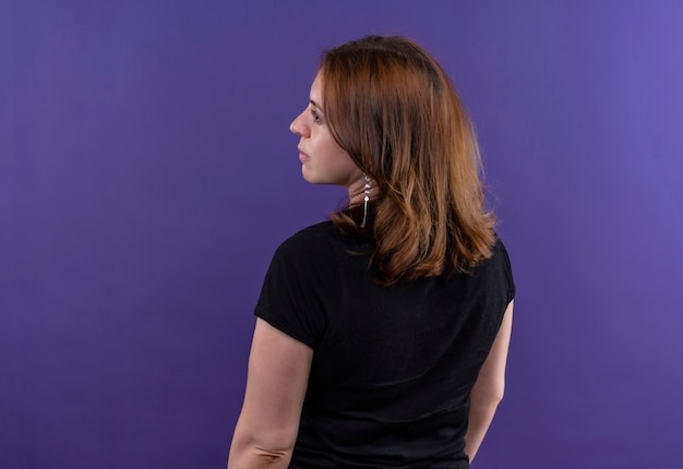 Jovem mulher casual em pé atrás da vista, olhando para o lado esquerdo em uma parede roxa isolada com espaço de cópia