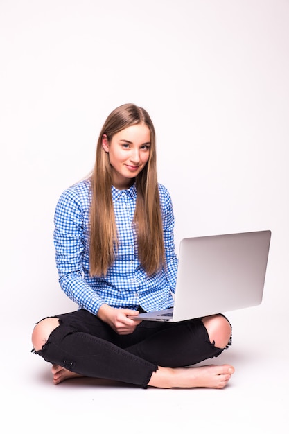 Jovem mulher casual sentada sorrindo segurando um laptop isolado na parede branca