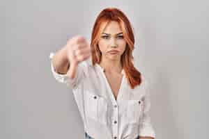 Foto grátis jovem mulher caucasiana em pé sobre fundo isolado, parecendo infeliz e zangado, mostrando rejeição e negativo com os polegares para baixo, gesto de má expressão