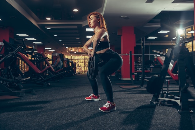 Jovem mulher caucasiana muscular praticando na academia com equipamento. Bem-estar, estilo de vida saudável, musculação.