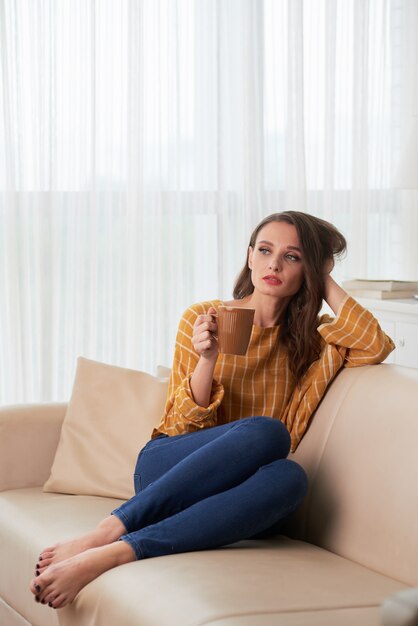 Jovem mulher caucasiana relaxando no sofá em casa com caneca