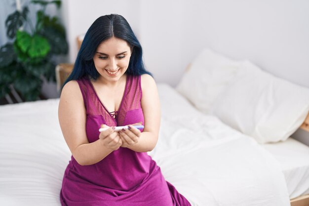 Jovem mulher caucasiana sorrindo confiante segurando o teste de gravidez no quarto