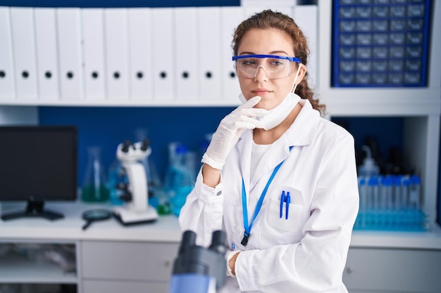 Foto grátis jovem mulher caucasiana trabalhando no laboratório cientista sorrindo olhando confiante para a câmera com braços cruzados e mão no queixo pensando positivo