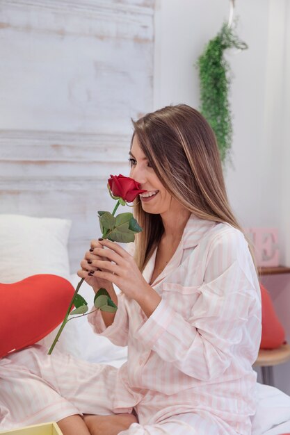 Jovem mulher cheirando rosa na cama