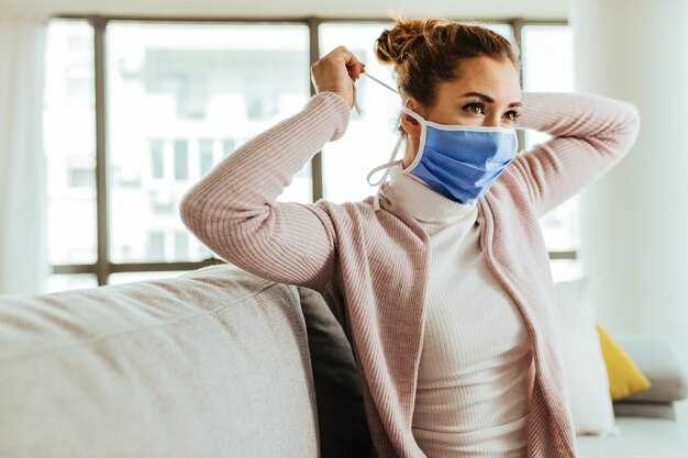 Jovem mulher colocando máscara facial enquanto está em casa durante a epidemia de vírus
