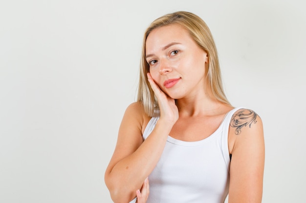 Foto grátis jovem mulher com a bochecha apoiada na palma da mão levantada em camiseta e parecendo alegre