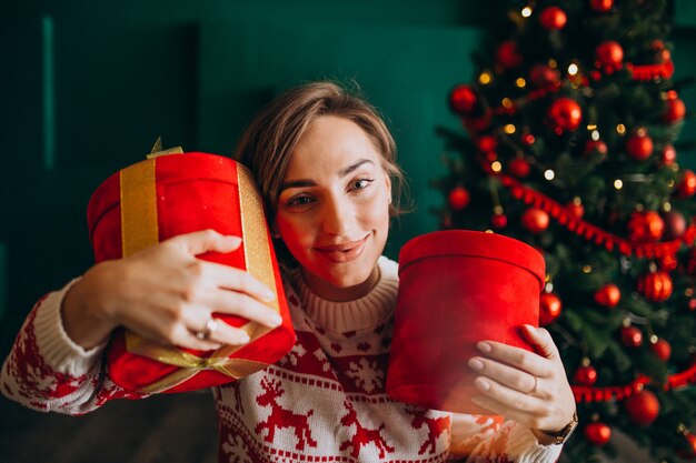 Jovem mulher com árvore de Natal segurando caixas vermelhas