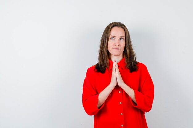 Jovem mulher com as mãos em gesto de oração na blusa vermelha e olhando pensativa. vista frontal.