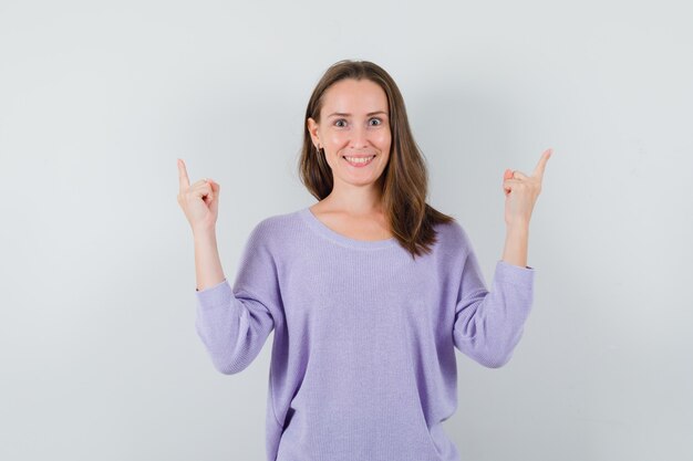 Jovem mulher com blusa lilás apontando para cima e parecendo alegre