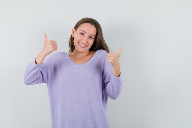 Jovem mulher com blusa lilás mostrando o polegar para cima e parecendo positivo