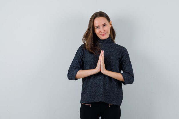 Foto grátis jovem mulher com blusa preta mostrando gesto namastê e parecendo feliz