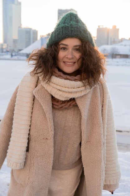 Jovem mulher com cabelo encaracolado escuro com um chapéu de inverno, vestido calorosamente, geada de inverno, dia ensolarado lá fora.