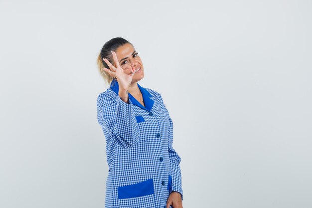 Jovem mulher com camisa de pijama guingão azul mostrando sinal de ok e bonita vista frontal