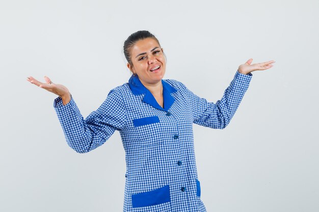 Jovem mulher com camisa de pijama guingão azul, mostrando um gesto impotente e bonita, vista frontal.