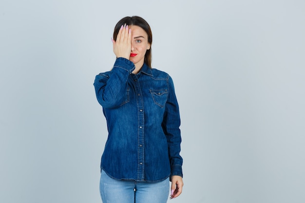 Foto grátis jovem mulher com camisa jeans e jeans segurando a mão no olho e parecendo uma fofa