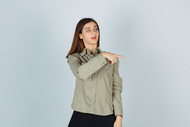 Foto grátis jovem mulher com camisa, saia apontando para a direita e olhando com foco, vista frontal.
