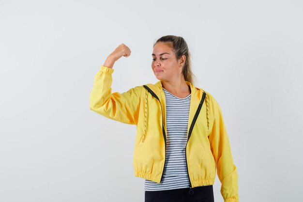 Jovem mulher com casaco, t-shirt mostrando o punho cerrado e parecendo confiante, vista frontal.