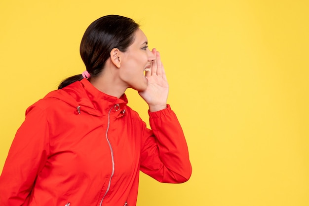 Jovem mulher com casaco vermelho chamando em fundo amarelo