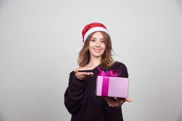 Jovem mulher com chapéu de Papai Noel, mostrando uma caixa de presente presente.