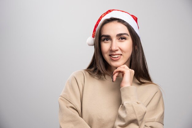 Jovem mulher com chapéu de Papai Noel posando estúdio tiro isolado em cinza.