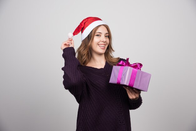 Jovem mulher com chapéu de Papai Noel segurando uma caixa de presente presente.