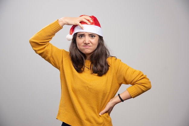 Foto grátis jovem mulher com chapéu de papai noel vermelho posando sobre uma parede branca.