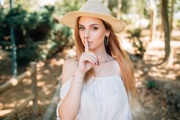 Jovem mulher com chapéu de verão com o dedo indicador nos lábios, peça para ficar quieta. Silêncio e conceito secreto