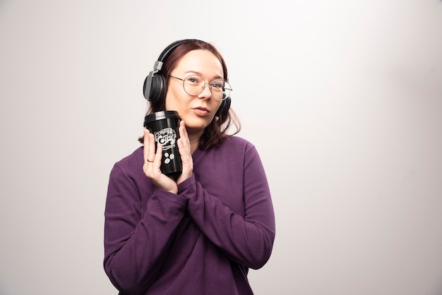 Jovem mulher com copo posando em fones de ouvido em um fundo branco. Foto de alta qualidade