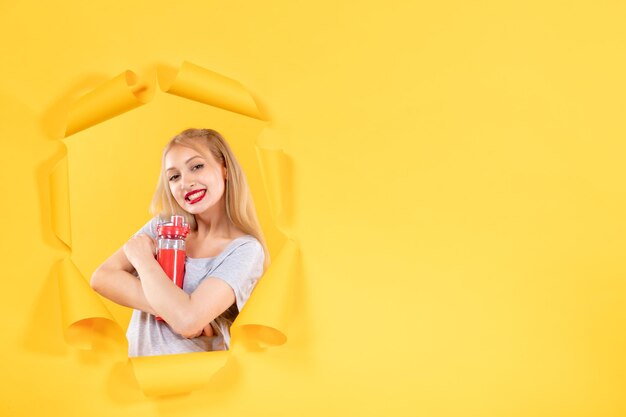 Jovem mulher com garrafa vermelha na parede amarela