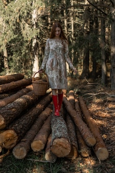 Jovem mulher com longos cabelos ruivos em um vestido de linho recolhendo cogumelos na floresta