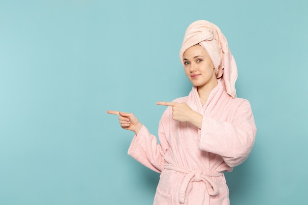 jovem mulher com roupão rosa após o banho, posando com um sorriso no azul